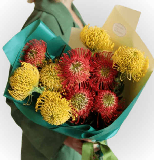Arabian Sunset Pincushion Bouquet with red and yellow pincushion proteas wrapped in green paper, showcasing vibrant blooms from a Dubai flower market