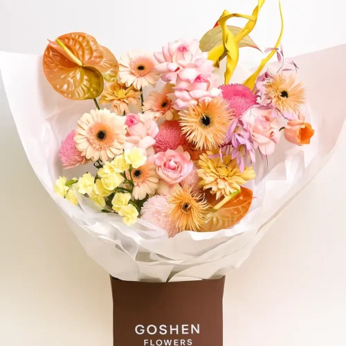Golden hour glow flower bouquet with anthuriums, calla lilies, and greenery in a brown gift bag – Goshen Flower Dubai.