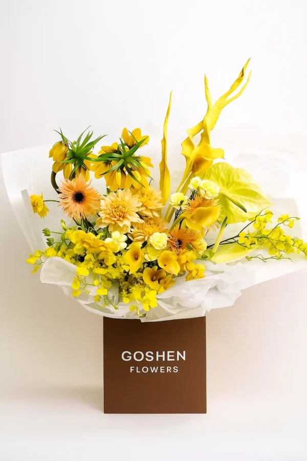 Sunburst Serenade is a bright yellow bouquet with orchids, calla lilies, and tropical flowers in a brown box – Goshen Flower UAE.