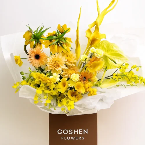 Sunburst Serenade a Bright yellow bouquet with orchids, calla lilies, and tropical flowers in a brown box – Goshen Flower UAE.